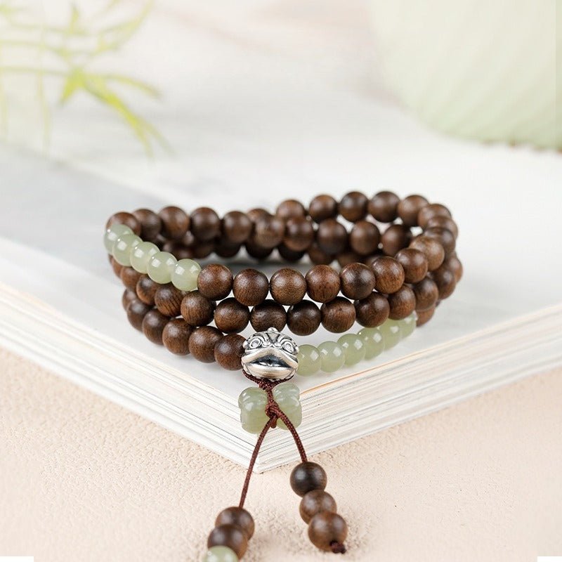 Courage and Fortune Lion Dance Charm Agarwood Bracelet - Serenity & Joy - front view on a book